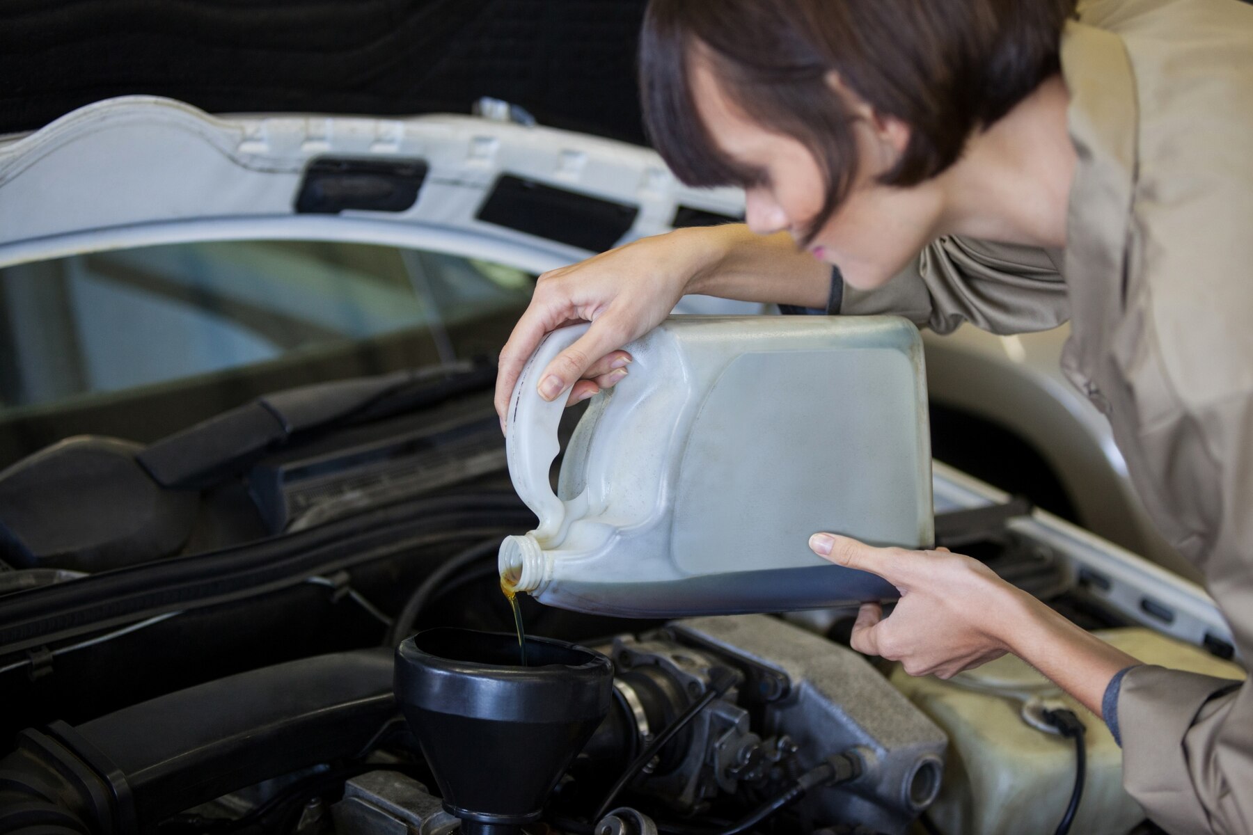 female mechanic pouring oil lubricant into car engine